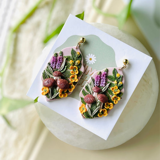 Explore nature’s charm with these polymer clay earrings! Adorned with purple lupines, yellow ranunculi, and cute brown button mushrooms, each pair is a whimsical delight.